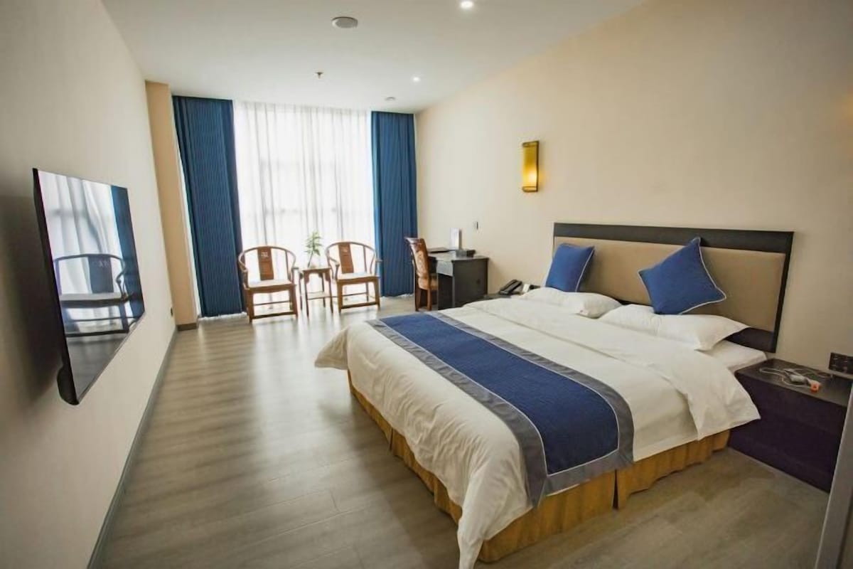 A hotel room with a large bed, a desk, a chair, and a TV.