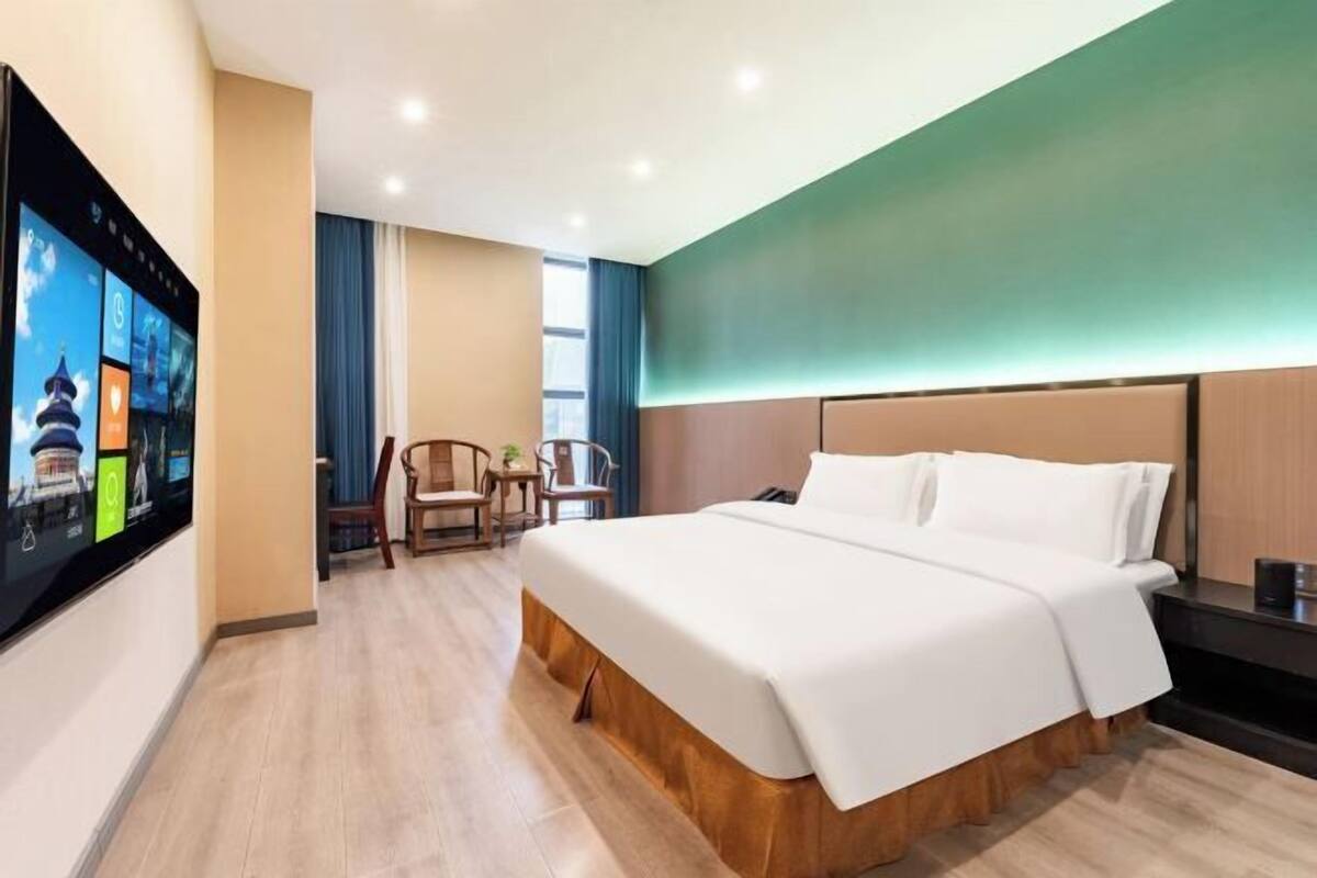 Ein modernes Hotelzimmer mit einem großen Bett, einem flachbildfernseher an der Wand, einem Holzkopfteil und einem kleinen Tisch mit Stühlen.