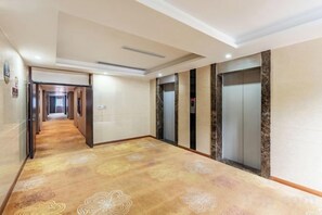 Pasillo de hotel con alfombra estampada, ascensores y una puerta al final.