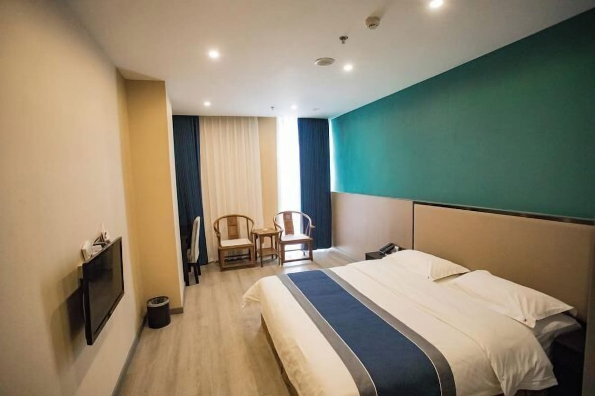 A hotel room with a bed, a desk, a chair, a TV, and a window with curtains.