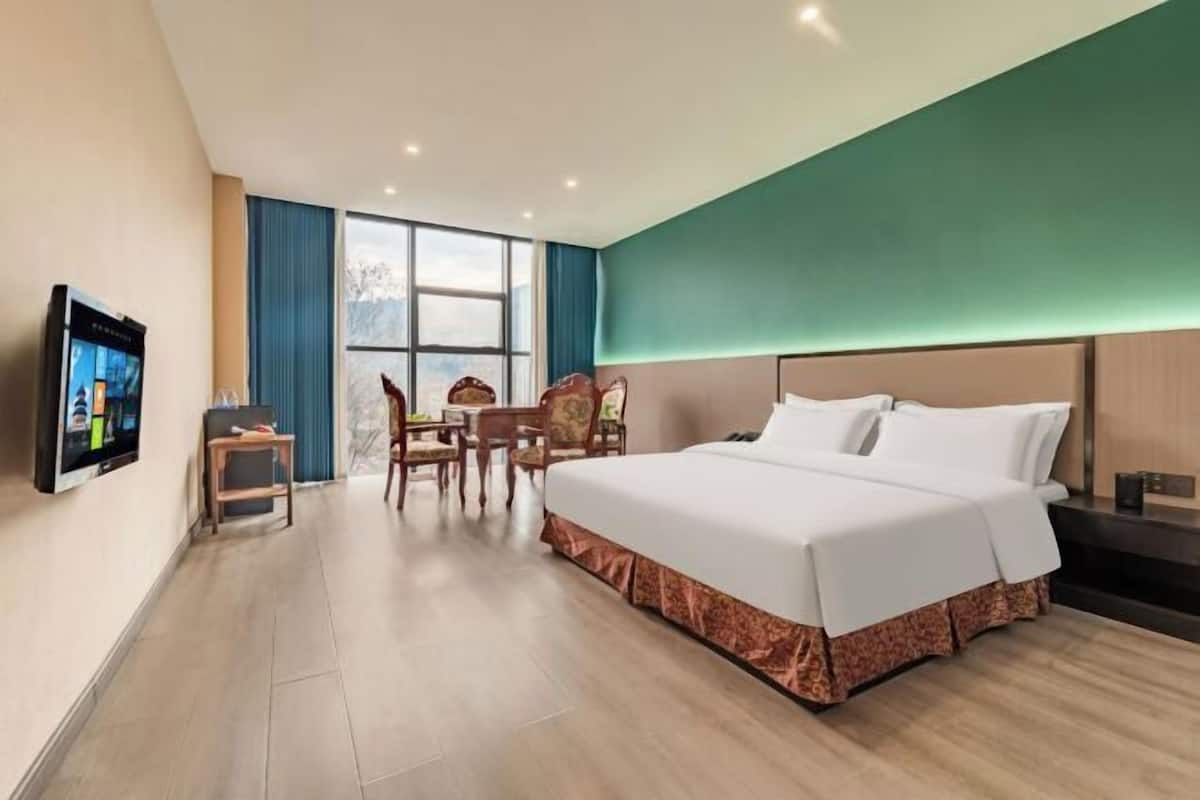 Ein Hotelzimmer mit einem großen Bett, einem Schreibtisch mit Stuhl, einem Fernseher und einem Fenster mit Vorhängen.