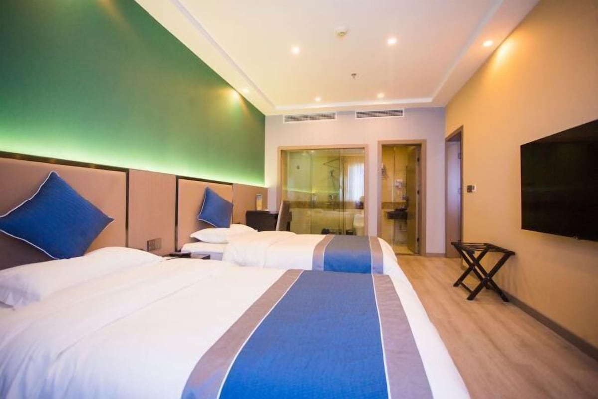 A hotel room with two beds, a TV, and a glass door leading to a bathroom.