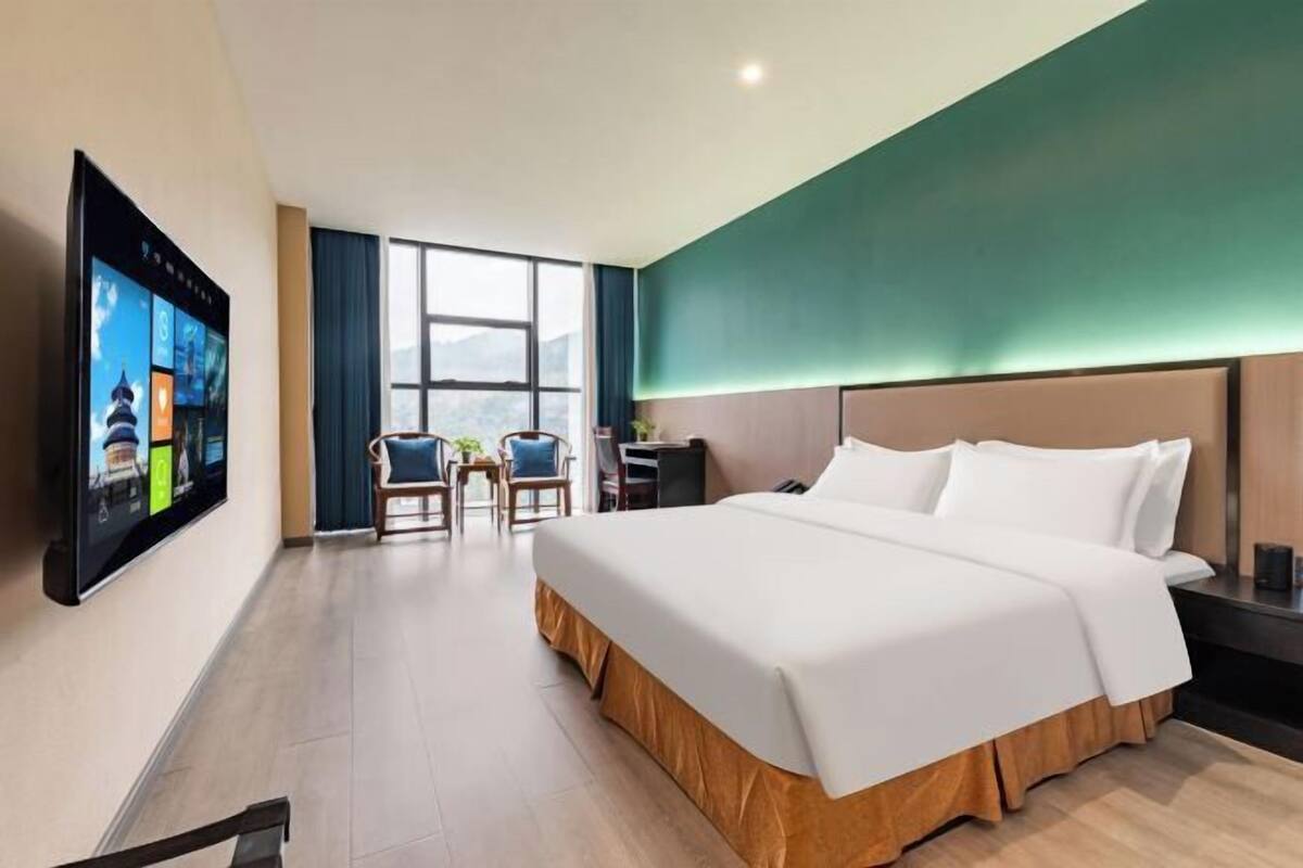 Ein Hotelzimmer mit einem großen Bett, einem Schreibtisch, einem Sessel und einem an der Wand befestigten Fernseher.