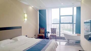 Quarto de hotel com uma cama grande, uma banheira e vista da cidade através de amplas janelas.