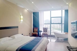 Habitación de hotel con una cama grande, una bañera y vistas de la ciudad a través de amplias ventanas.
