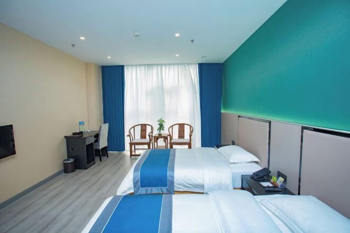 A hotel room with two beds, a desk, chairs, a TV, and a window with curtains.