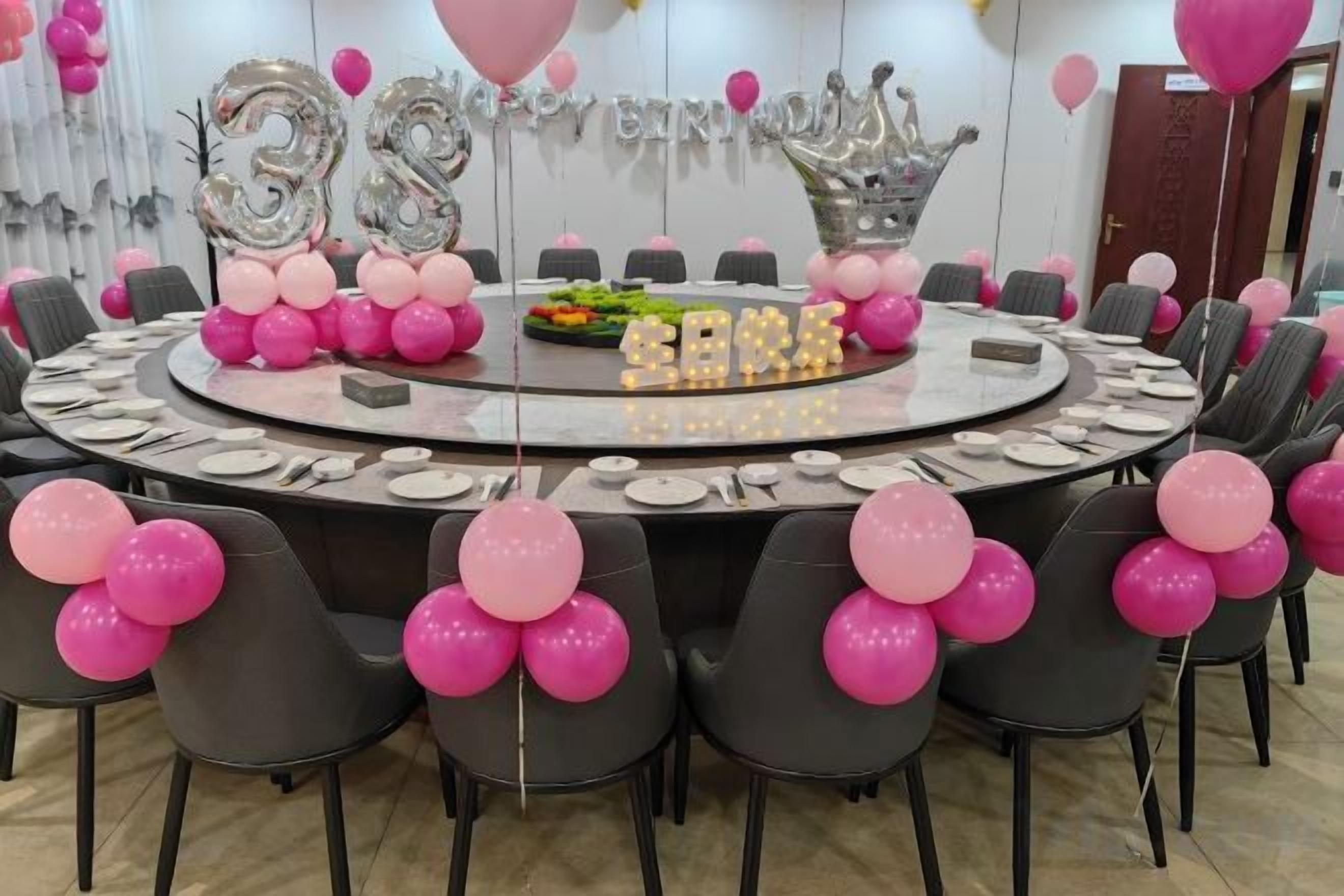 Mesa redonda com balões cor de rosa e balões prateados, e um letreiro com o número '35'.