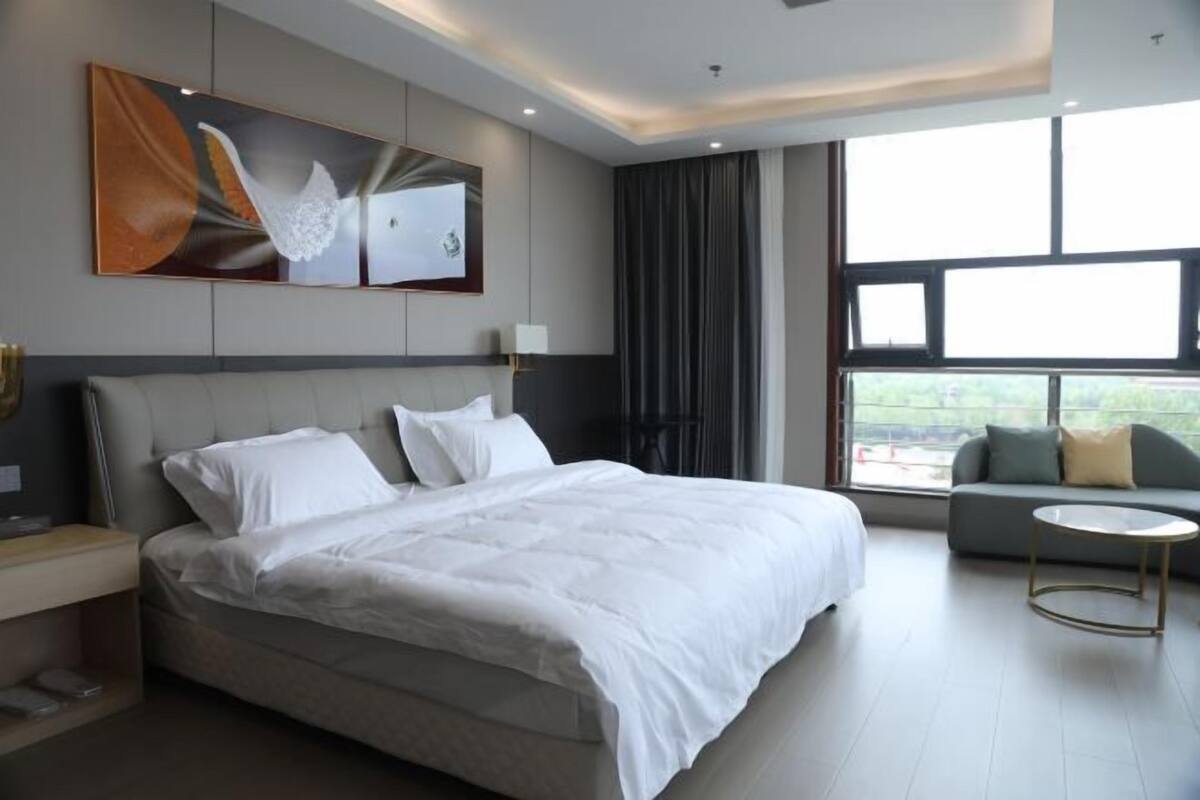 Une chambre d’hôtel moderne, dotée d’un grand lit, d’un canapé, d’une petite table ronde et d’une grande fenêtre donnant sur l’extérieur.