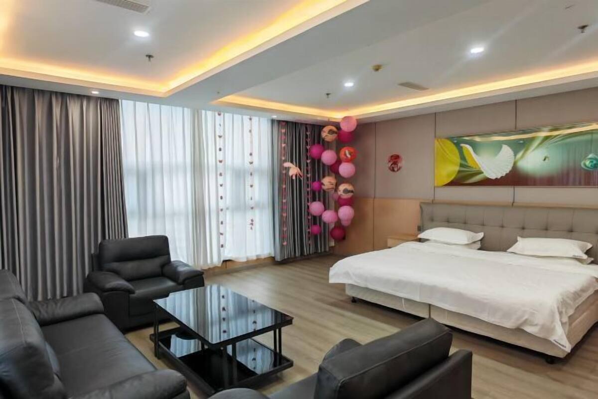 Une chambre d’hôtel moderne, dotée d’un grand lit, d’un canapé, d’une table basse et d’un mur orné d’une fresque décorative.