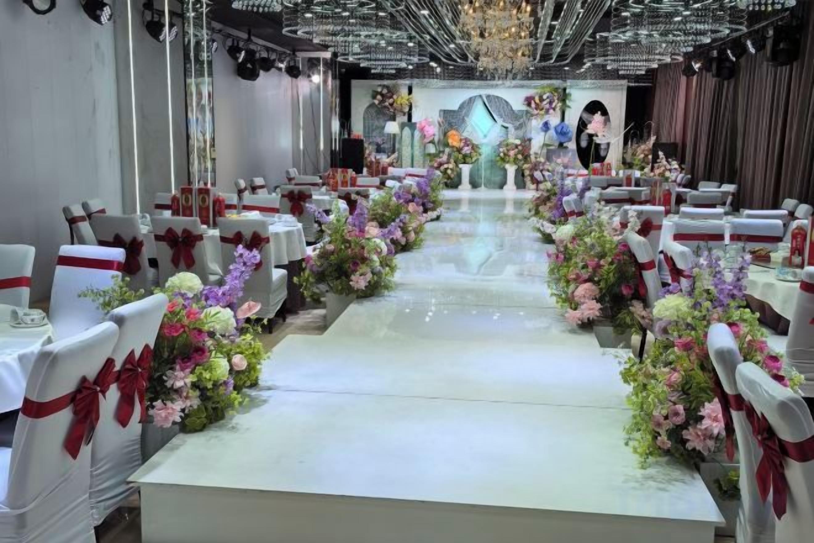Ein Bankettsaal mit Tischen und Stühlen, einer Bühne im Vordergrund und Blumendekorationen.