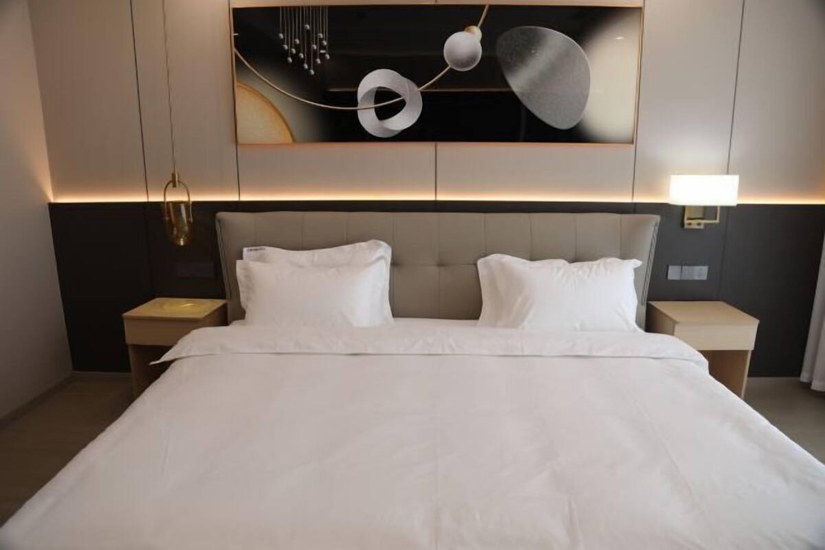 Une chambre d’hôtel avec un grand lit, deux tables de chevet et une œuvre d’art moderne accrochée au mur au-dessus du lit.