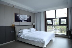 Quarto moderno com uma cama grande, vista para o exterior através de uma janela e um quadro na parede.
