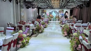 A banquet hall with white tables and chairs, each adorned with red sashes. The tables are decorated with floral arrangements. - Fenghuangtai Holiday Hotel Junan Lingang Development Zone (Junan County)