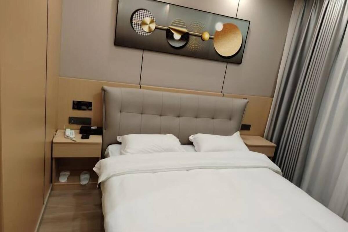 Une chambre d’hôtel avec un grand lit, une tête de lit, une table de chevet, une œuvre d’art accrochée au mur et un rideau.