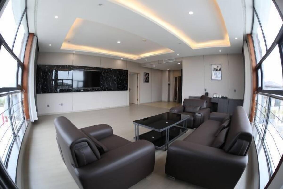 Un vaste espace de vie au design moderne, comprenant un grand mur en marbre noir, une table basse en verre et un coin salon avec des canapés en cuir.