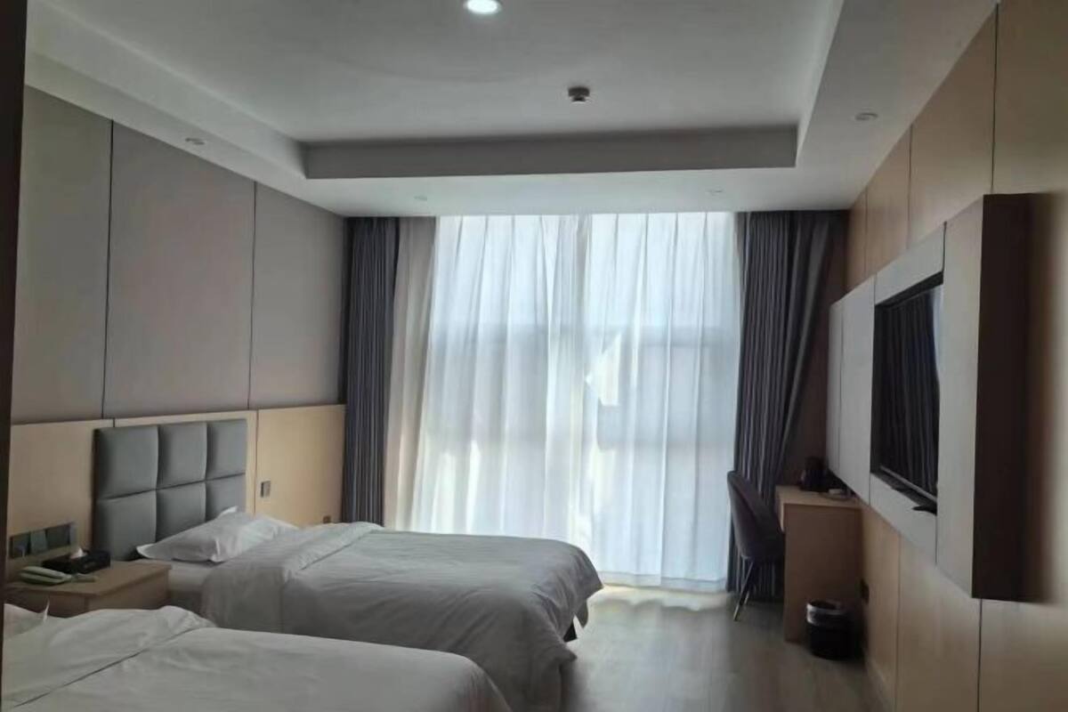 Une chambre d’hôtel avec deux lits, un bureau, une chaise, une télévision et une grande fenêtre avec des rideaux.