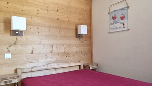 Un dormitorio con cabecera de madera, colcha roja, dos mesitas de noche y dos apliques de pared.