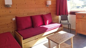 Habitación de cabaña de madera con sofá, una mesita, una silla y vistas a un paisaje montañoso.