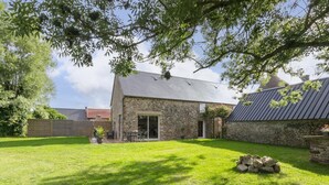 A stone house with a sloped roof, a grassy yard, and a wooden fence. - Single-storey house in Anneville sur Mer with private garden (Gouville-sur-Mer)