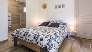 A bedroom with a wooden bed, a bedside table with a lamp, and a door. - Single-storey house in Anneville sur Mer with private garden (Gouville-sur-Mer)