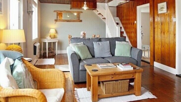 A cozy living room with a grey sofa, wicker chair, wooden coffee table, and a staircase leading to another level. - Charming original fisherman’s cottage on Dungeness Beach (Lydd)
