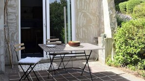 Eine Terrasse mit Tisch und Stühlen, eine Schale auf dem Tisch und eine Schiebetür zu einem Innenbereich.
