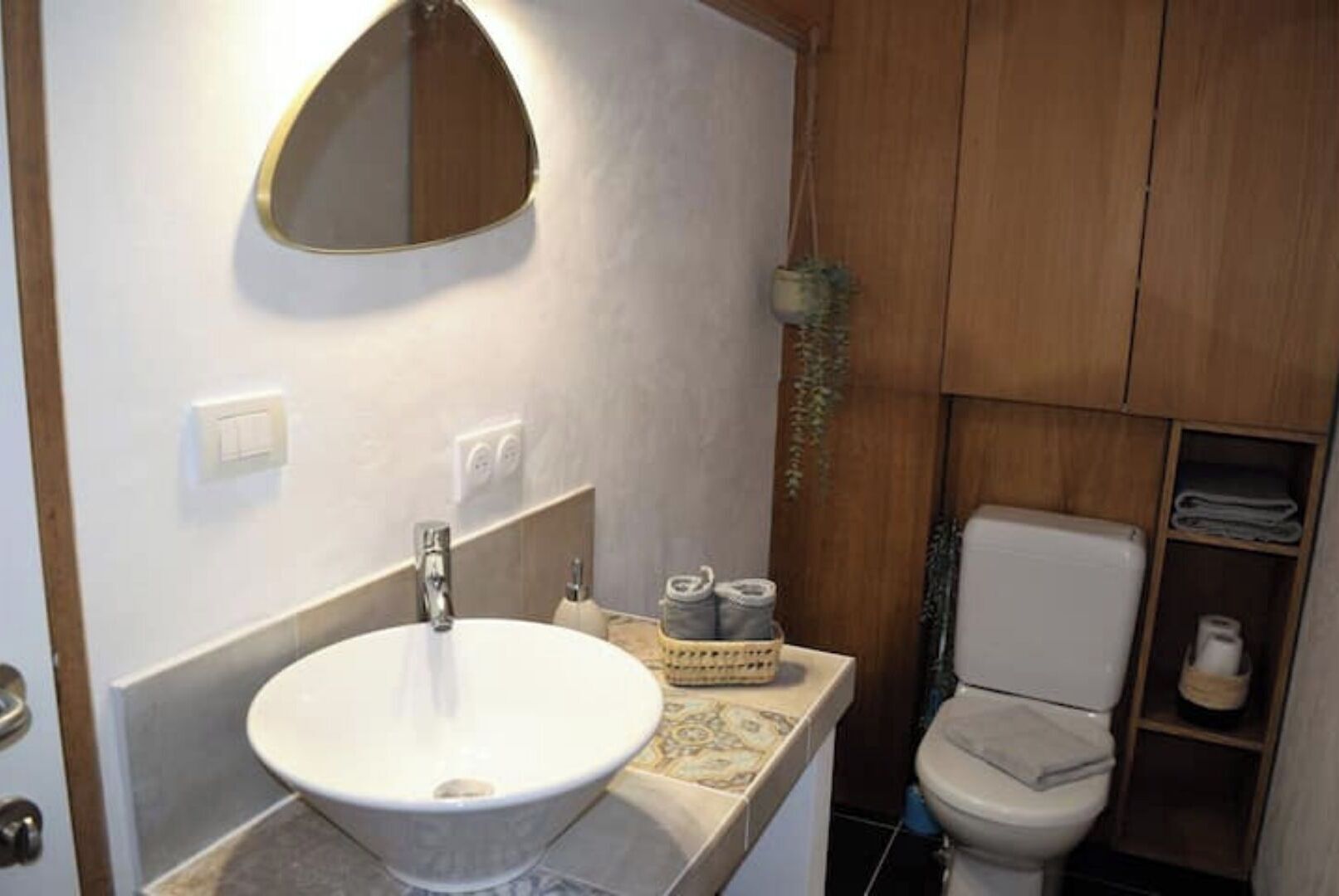 Une salle de bain avec un lavabo blanc, un miroir, des toilettes et des meubles en bois.