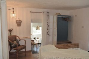Um quarto com cama, uma cadeira, uma mesinha e um guarda-roupa.