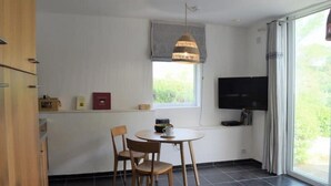 Ein Zimmer mit Esstisch, Stühlen, Fernseher und einem Fenster mit Vorhängen.