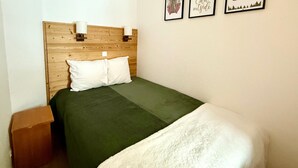 Un lit avec une tête de lit en bois, une couvre-lit verte et une couverture blanche. Trois tableaux encadrés sont accrochés au mur.