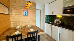 Une cuisine compacte aux murs en bois, une table à manger pour quatre personnes et des appareils électroménagers modernes.