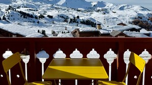 Une table et des chaises jaunes sur un balcon donnant sur un paysage montagneux enneigé.