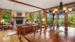Un salón amplio con chimenea, muebles de madera y ventanas grandes que ofrecen vistas al exterior.