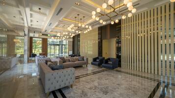 A spacious lobby with a high ceiling, modern chandeliers, and a seating area with sofas and armchairs.