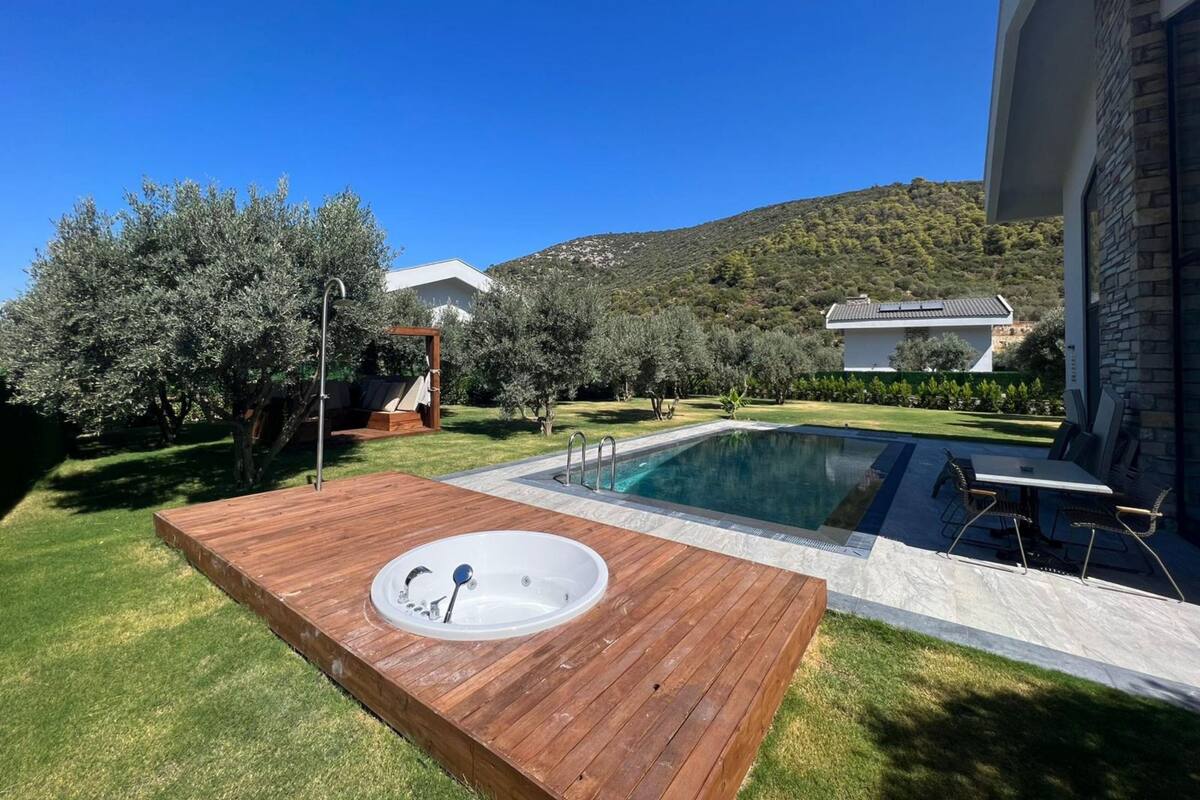 Ein Poolbereich mit Whirlpool, Holzterrasse und Blick auf ein Haus und Berge.