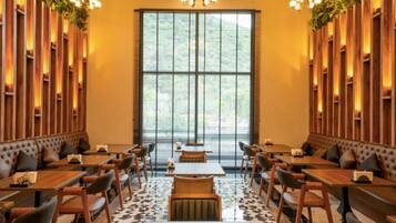 Un restaurante con paneles de madera, ventanas grandes y una araña. Mesas y sillas dispuestas para comer.