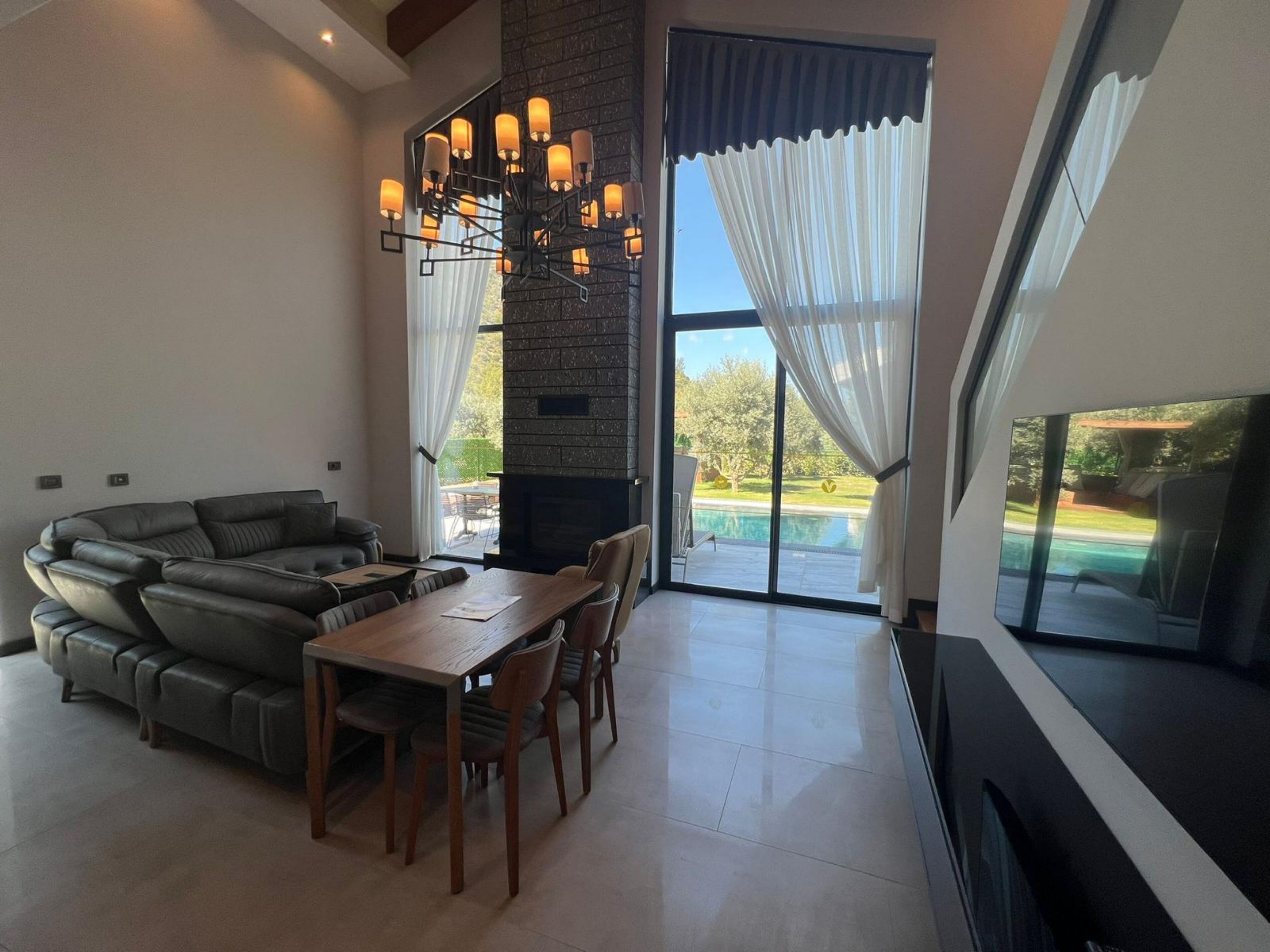 Una sala de estar moderna con un sofá modular, una mesa de comedor, sillas, una chimenea y un amplio ventanal corredera que da a una piscina.