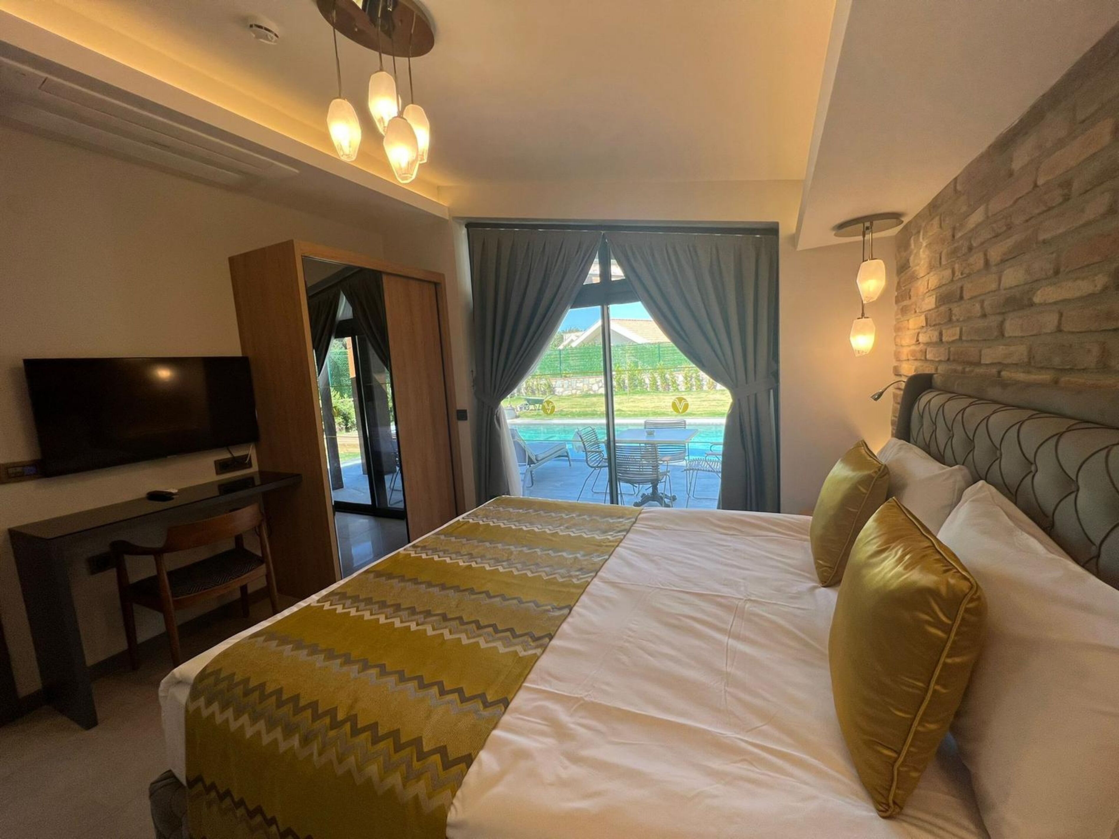 Een hotelkamer met een bed, een bureau, een televisie en uitzicht op een zwembad en tuin.