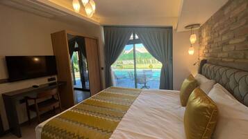 Een hotelkamer met een bed, een bureau, een televisie en uitzicht op een zwembad en tuin.