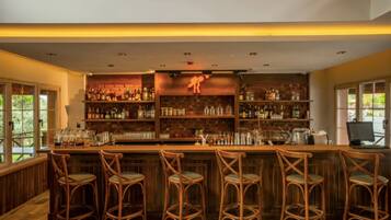 A bar area with wooden bar stools, shelves stocked with bottles, and a large window on the left.