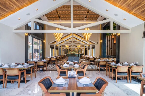 A spacious restaurant with high ceilings, wooden beams, and modern chandeliers. Tables are neatly arranged with chairs, and the floor is marble. - Batıhan Vadi Hotel (Kusadasi)