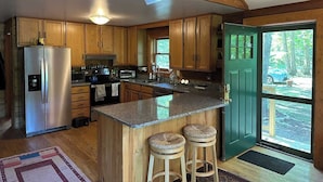 A kitchen with wooden cabinets, a stainless steel refrigerator, a granite countertop, and a green door leading outside.