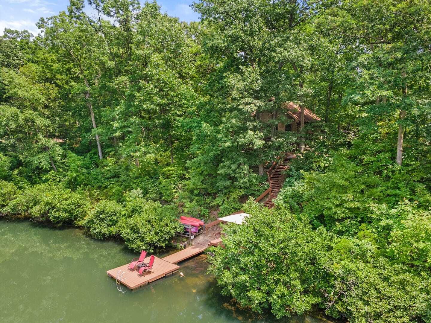 Un muelle de madera se extiende sobre un río rodeado de abundante vegetación, con una escalera que lleva a una cabaña.