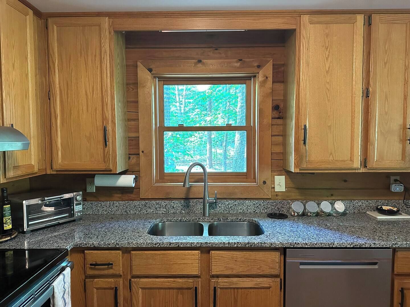A kitchen with wooden cabinets, a double sink, a built-in oven, and a window with a view of trees.