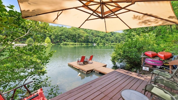 A wooden deck with a table and chairs, a floating dock, and an umbrella providing shade.