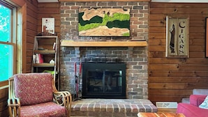 A cozy living room with a brick fireplace, a wooden mantel, and a bookshelf.