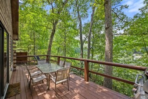 A wooden deck with a glass table and chairs, surrounded by trees and a view of a lake. - Rustic Log Cabin with Private Dock on the Lake! (Harpers Ferry)