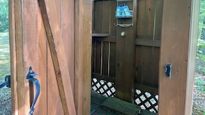 A wooden outdoor toilet with a metal rack holding cleaning supplies.