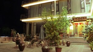 Un edificio de dos pisos con una entrada bien iluminada, zona de estar al aire libre y plantas en macetas.