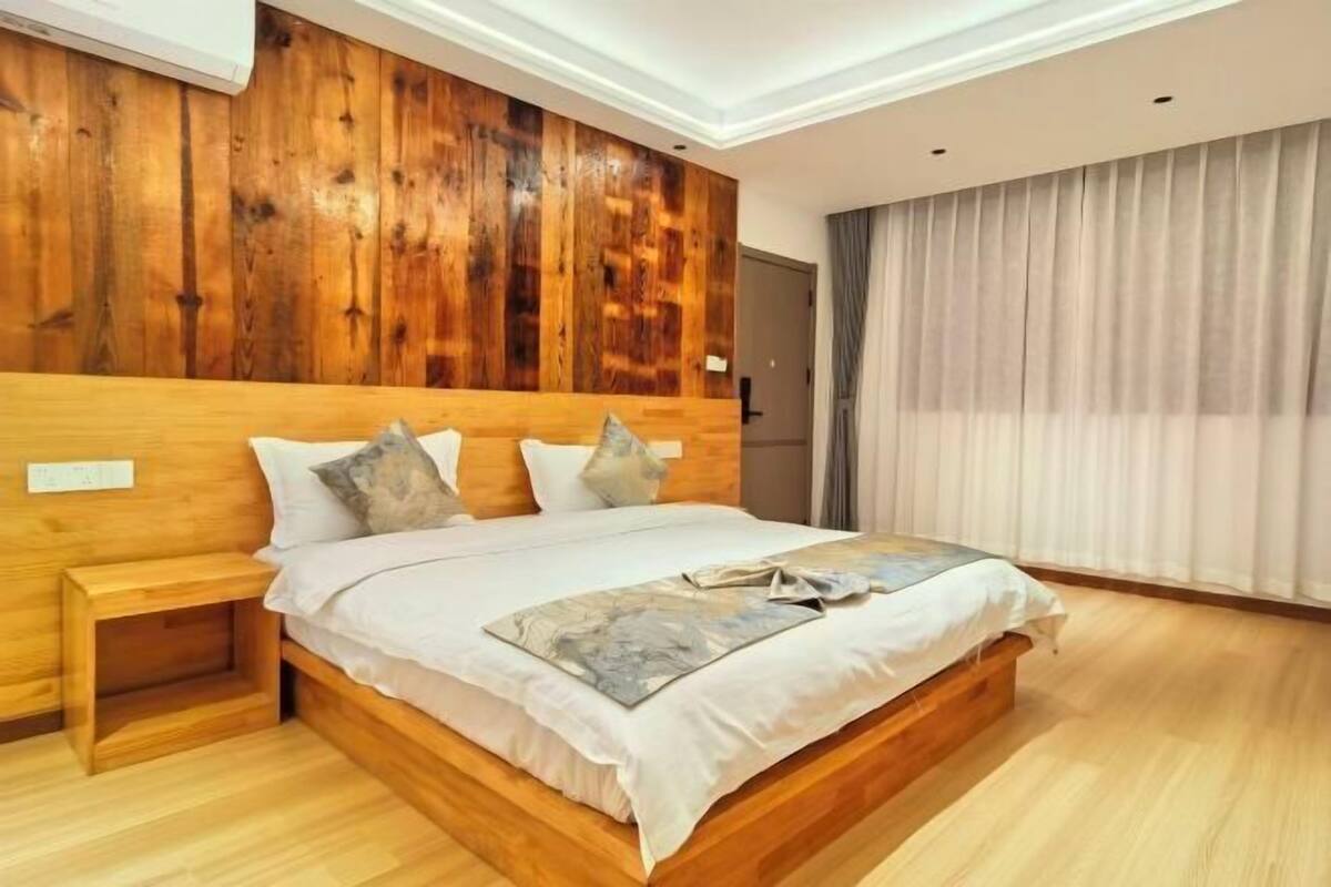 A bedroom with a wooden headboard, a bed with white bedding, a nightstand, and a window with curtains.